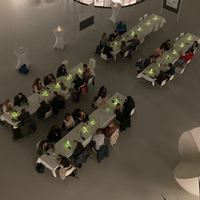 Overhead view of people seated at long tables with green-lit centerpieces in a large room.