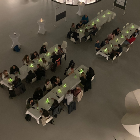 Overhead view of people seated at long tables with green-lit centerpieces in a large room.